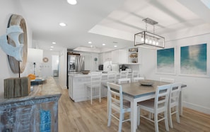 A modern kitchen with white cabinetry, a central island, and a dining area with white chairs.