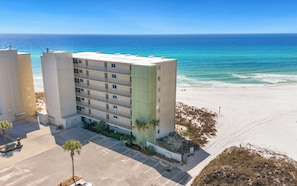 A multi-story hotel with a beach view, parking lot, and a sandy beach area.
