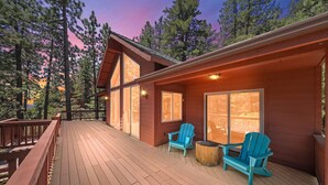 A wooden deck with two chairs and a table, surrounded by tall trees and a sunset sky. - Mountain View: Gorgeous Views, AC, Jacuzzi bathtub! (Idyllwild)