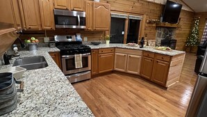 Eine Küche mit Holzausstattung, Granit Arbeitsplatten, Edelstahlgeräten und einem Kamin aus Stein.