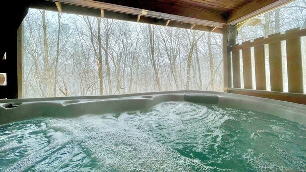 Ein Whirlpool mit Blick auf eine durch ein Holzdeck sichtbare, kahlstehende Baumlandschaft.