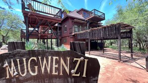A rustic wooden building with multiple balconies and a covered outdoor seating area, surrounded by greenery. - Kruger Kumba - Mugwenzi (Marloth Park)