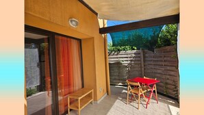 Un patio cubierto con una mesa y sillas de madera, además de un banco y un gran ventanal corredizo.