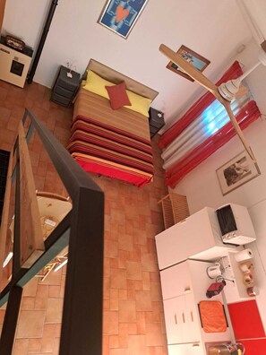 Une chambre à coucher avec un lit, une table de chevet, une lampe, un radiateur et une fenêtre avec des rideaux.