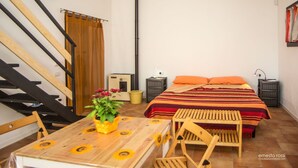 Un dormitorio con cama, muebles de madera, una mesa con planta, una escalera y un calefactor.