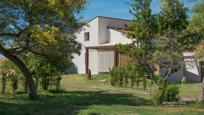 Una casa moderna con un garaje grande, rodeada de árboles y un patio cubierto de césped.