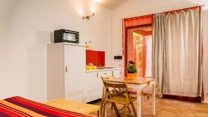 Una habitación pequeña con cama, un escritorio, una silla, microondas, lavamanos y ventana con cortinas.