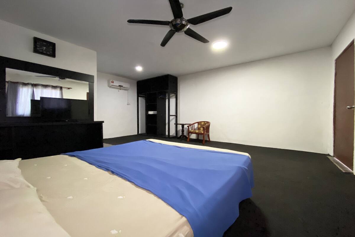 A hotel room with a bed, a ceiling fan, a desk, a chair, and a door.