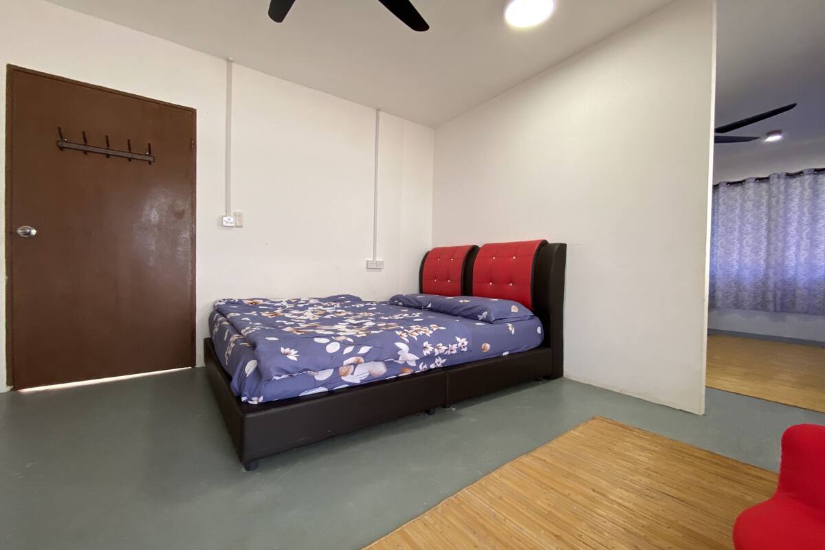 A bedroom with a bed, a wooden floor, a red chair, and a ceiling fan.