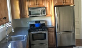 Une cuisine dotée de meubles en bois, d’un réfrigérateur en acier inoxydable, d’un four à micro-ondes, d’une cuisinière et d’un ventilateur de plafond.