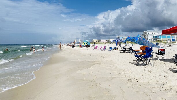 A beach with a sandy shore, umbrellas, and beach chairs. - Spacious condo, fully furnished! Steps from white sugary sand of Gulf Shores! (Gulf Shores)