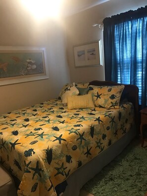 Un dormitorio con una cama con colcha de motivos marinos, un cuadro en la pared y una ventana con cortinas azules.