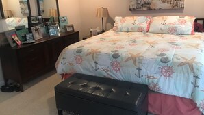 A bedroom with a bed, a dresser, a mirror, and a painting of a beach scene. - Spacious condo, fully furnished! Steps from white sugary sand of Gulf Shores! (Gulf Shores)