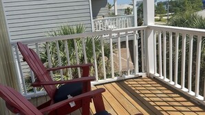 A wooden deck with two red Adirondack chairs, a white railing, and a building in the background. - Spacious condo, fully furnished! Steps from white sugary sand of Gulf Shores! (Gulf Shores)