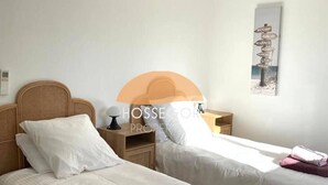 A hotel room with two beds, a nightstand, a lamp, and a wall-mounted sign. - Appt Ortolans - Hossegor center - Terrace - Park (Soorts-Hossegor)