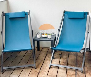 Two blue canvas chairs with metal frames, a small table with white cups and a decorative item, and a wooden floor.