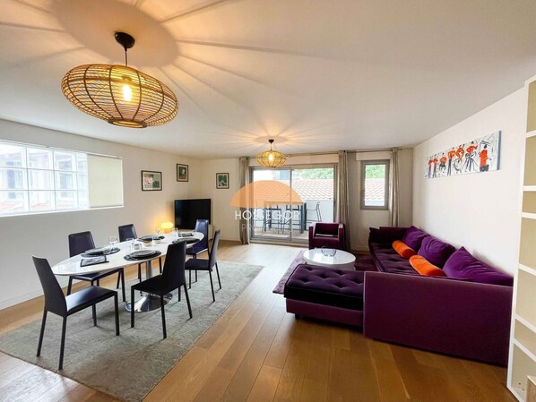 A modern living room with a dining area, a purple sofa, a round coffee table, and a large window.