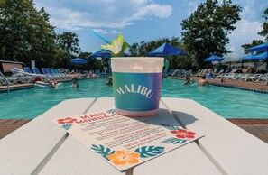 Et poolmiljø med et drikkeglas mærket "MALIBU" og en menu der viser hawaiiansk inspireret mad.
