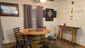A round wooden table with chairs, a dartboard, and a small wooden cabinet with a rope ladder.