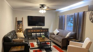 A living room with a sofa, armchair, coffee table, TV, and decorative items.