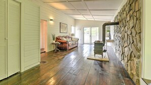 A spacious room with wooden floors, a stone wall, a leather sofa, and a large window. - Watauga River Cottage in Johnson City, TN! (Johnson City)