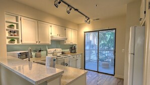 A modern kitchen with white cabinets, a marble countertop, and a sliding glass door leading to a balcony. - Walk to the Beach from this New Bright 2BR/2B condo in the <3 of The Island  (Hilton Head Island)