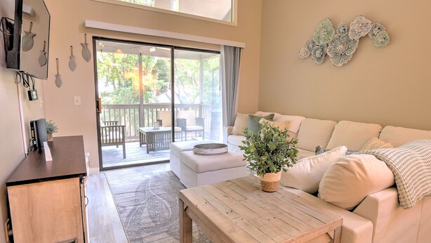 A modern living room with a sofa, a coffee table, and a sliding glass door leading to an outdoor patio. - Walk to the Beach from this New Bright 2BR/2B condo in the <3 of The Island  (Hilton Head Island)