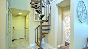 A spiral staircase with a modern design, a door at the bottom, and a wall clock. - Walk to the Beach from this New Bright 2BR/2B condo in the <3 of The Island  (Hilton Head Island)