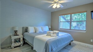 A bedroom with a bed, a nightstand, a ceiling fan, and a window with blinds. - Walk to the Beach from this New Bright 2BR/2B condo in the <3 of The Island  (Hilton Head Island)