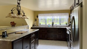 Una cocina con armarios de madera oscura, encimera de mármol, refrigerador de acero inoxidable y ventana con vista a la vegetación.