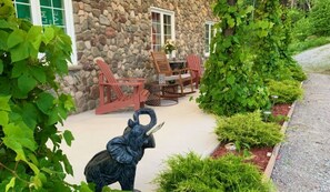 A stone building with a patio area featuring red Adirondack chairs and a small table. - Carriage House on 9.5 Acres.  Sit at the ocean or enjoy the waterfalls - Luxury (Bayside)