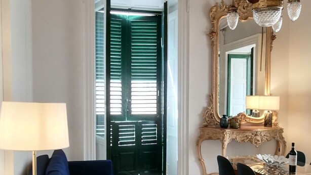Una stanza con un divano blu, un tavolo da pranzo con sedie, una lampada e uno specchio con cornice decorata.