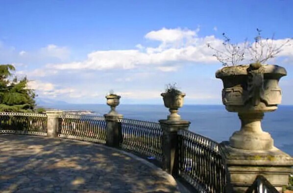 Une balustrade en pierre ornée de vases décoratifs, surplombant une étendue d’eau.