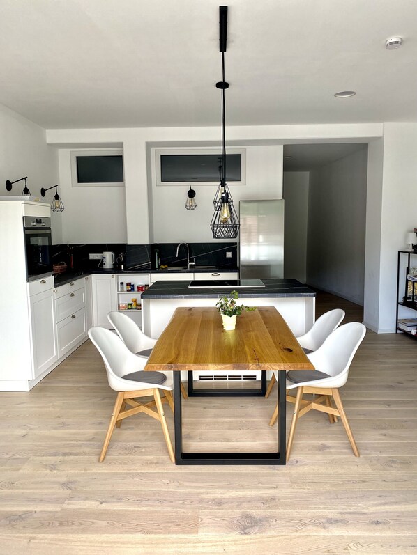 A modern kitchen with white cabinets, a wooden dining table, and two white chairs. - Exclusive 2-room loft apartment in Titisee-Neustadt (Titisee-Neustadt)