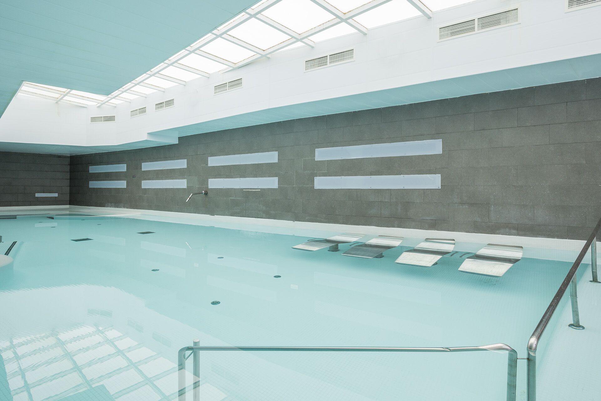 Una piscina interior con techo transparente, paredes con azulejos y una barrera de cristal.