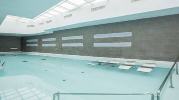 Una piscina interior con techo transparente, paredes con azulejos y una barrera de cristal.