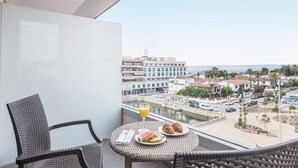 Un balcón con mobiliario de mimbre, una mesa de vidrio y vistas a un pueblo costero con edificios y un puerto deportivo.