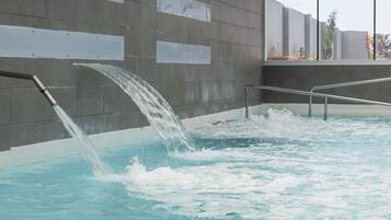 A modern indoor pool with a water feature, concrete walls, and metal railings.