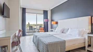 A hotel room with a large bed, a desk, and a chair. There is a TV mounted on the wall, and a balcony with a view of the city.