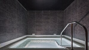 Un baño moderno con tonos oscuros, una bañera cuadrada, un pasamanos metálico y piso de baldosas.