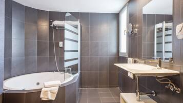 Ein modernes Badezimmer mit einer freistehenden Badewanne, einem Waschtisch mit Spiegel und dunkel gefliesten Wänden.