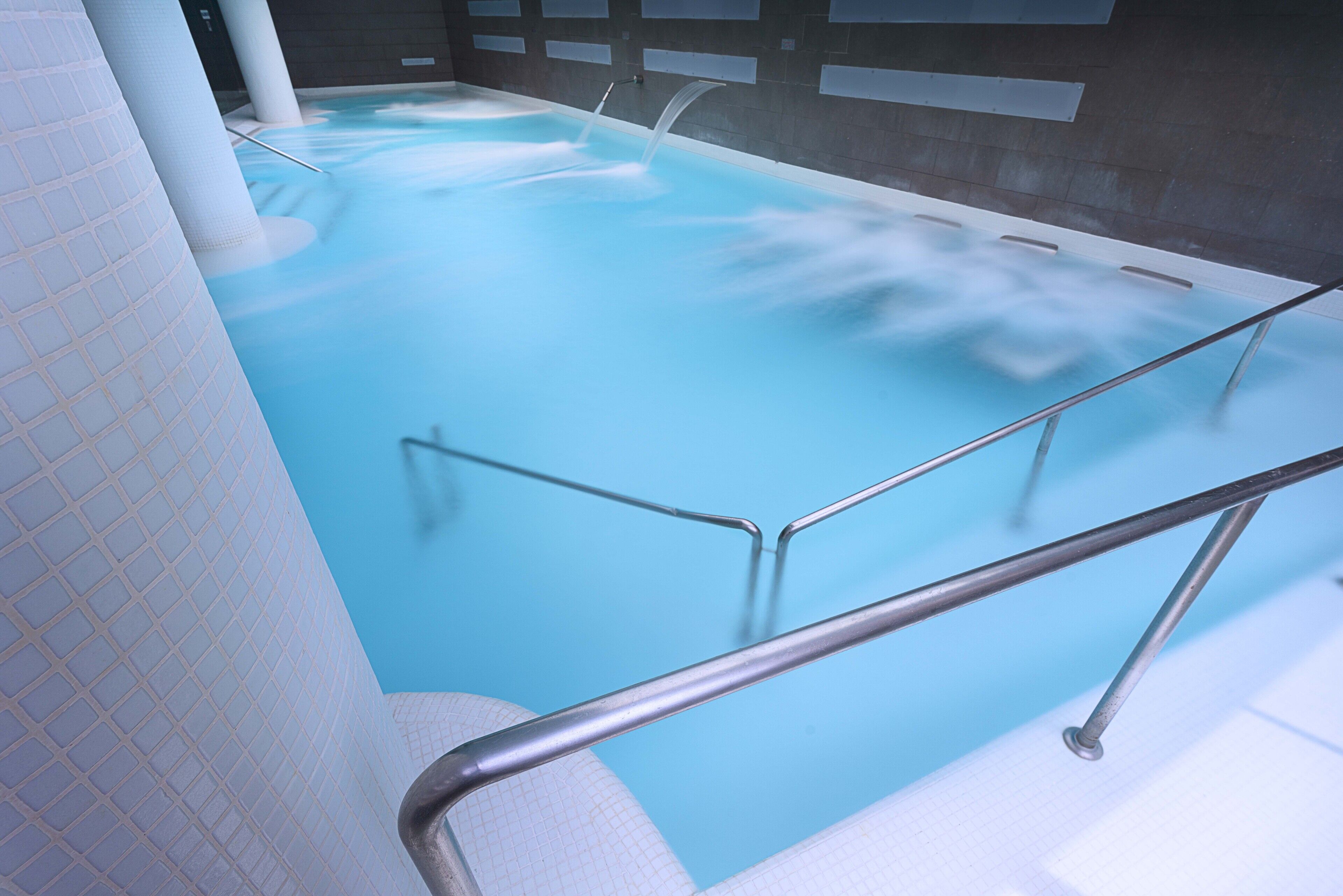 A modern indoor swimming pool with clear water, metal railings, and a tiled wall.