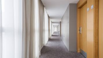 A hotel corridor with a carpeted floor, white walls, and a wooden door on the right.