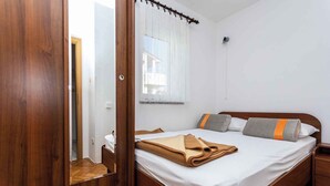 A bedroom with a wooden bed, white bedding, and a window with sheer curtains. - Holiday apartment with a view of the mountains (Baška)