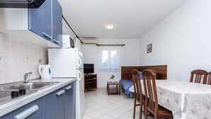 A compact kitchen with a sink, stove, and microwave. There is a dining table with chairs and a small TV. - Holiday apartment with a view of the mountains (Baška)