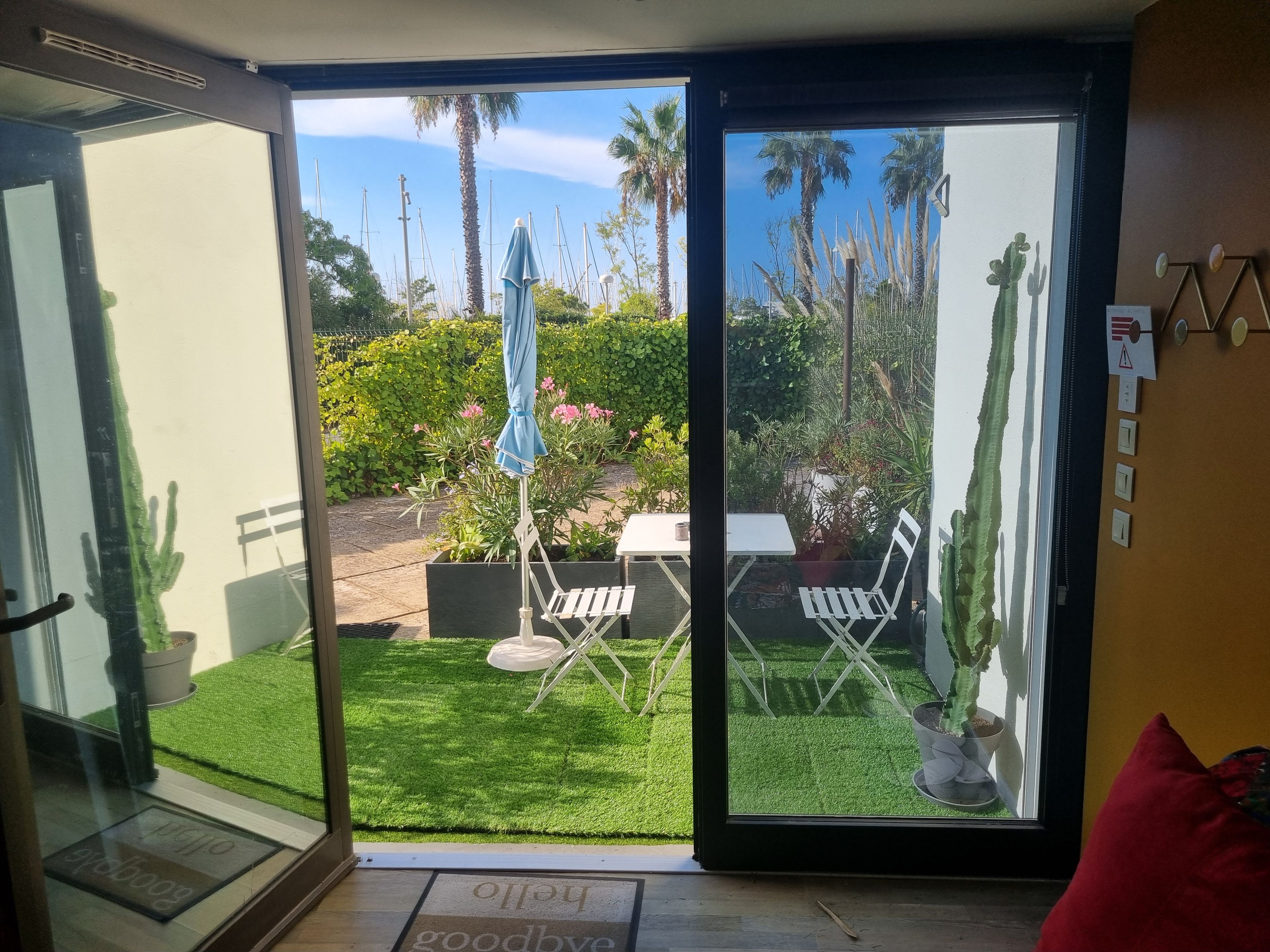 Une porte vitrée donnant sur un patio équipé d’une table, de chaises et de plantes en pot.