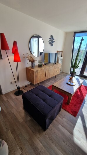 A modern living room with a wooden cabinet, a round mirror, a red floor lamp, a black ottoman, and a dining table with a red rug.