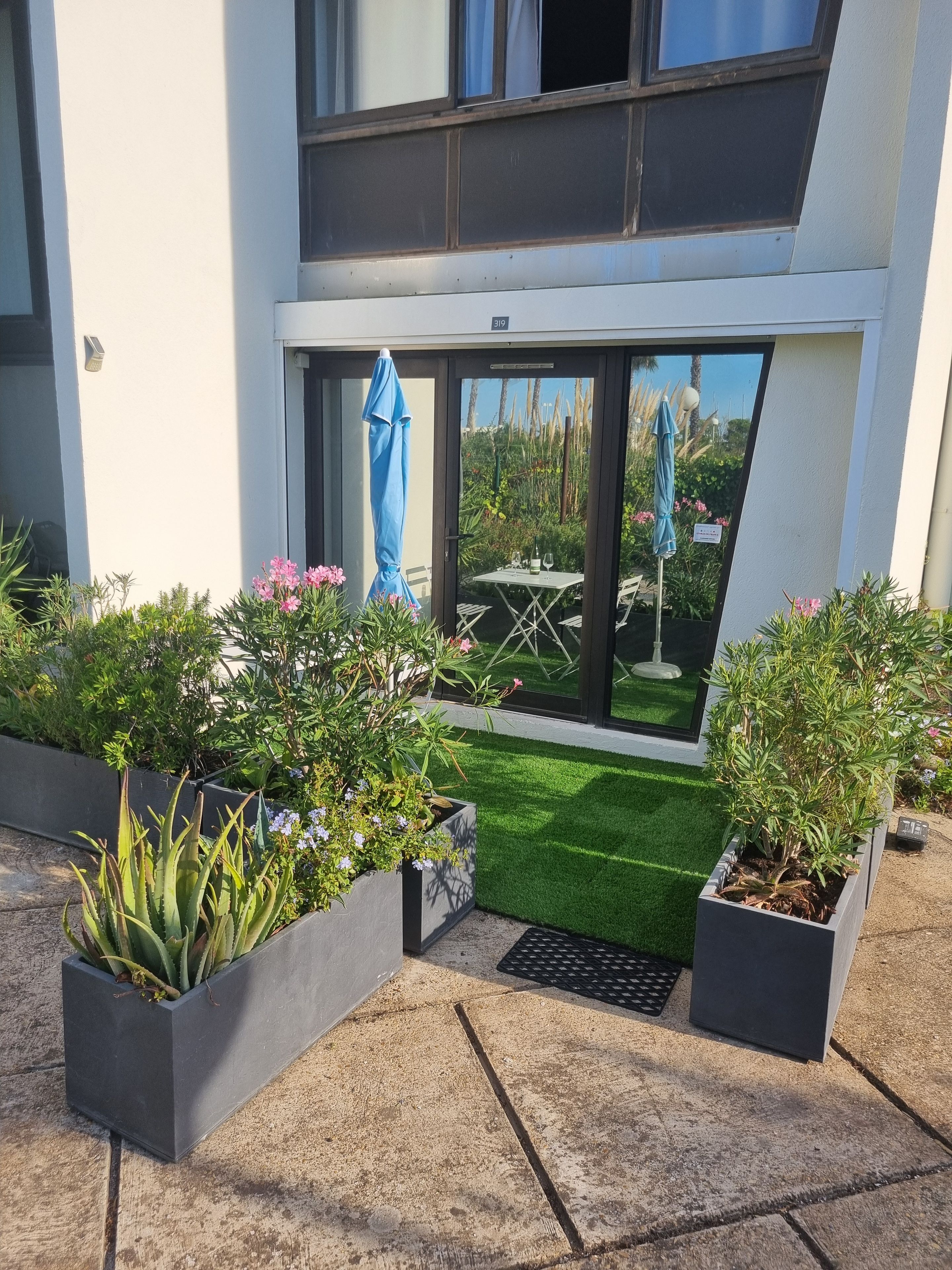 A modern outdoor area with a small lawn, potted plants, and a table with chairs.