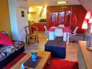 Ein Wohnzimmer mit einer Couch, einem Holztisch, einem Kaktus in einem blauen Topf und einem roten Teppich.