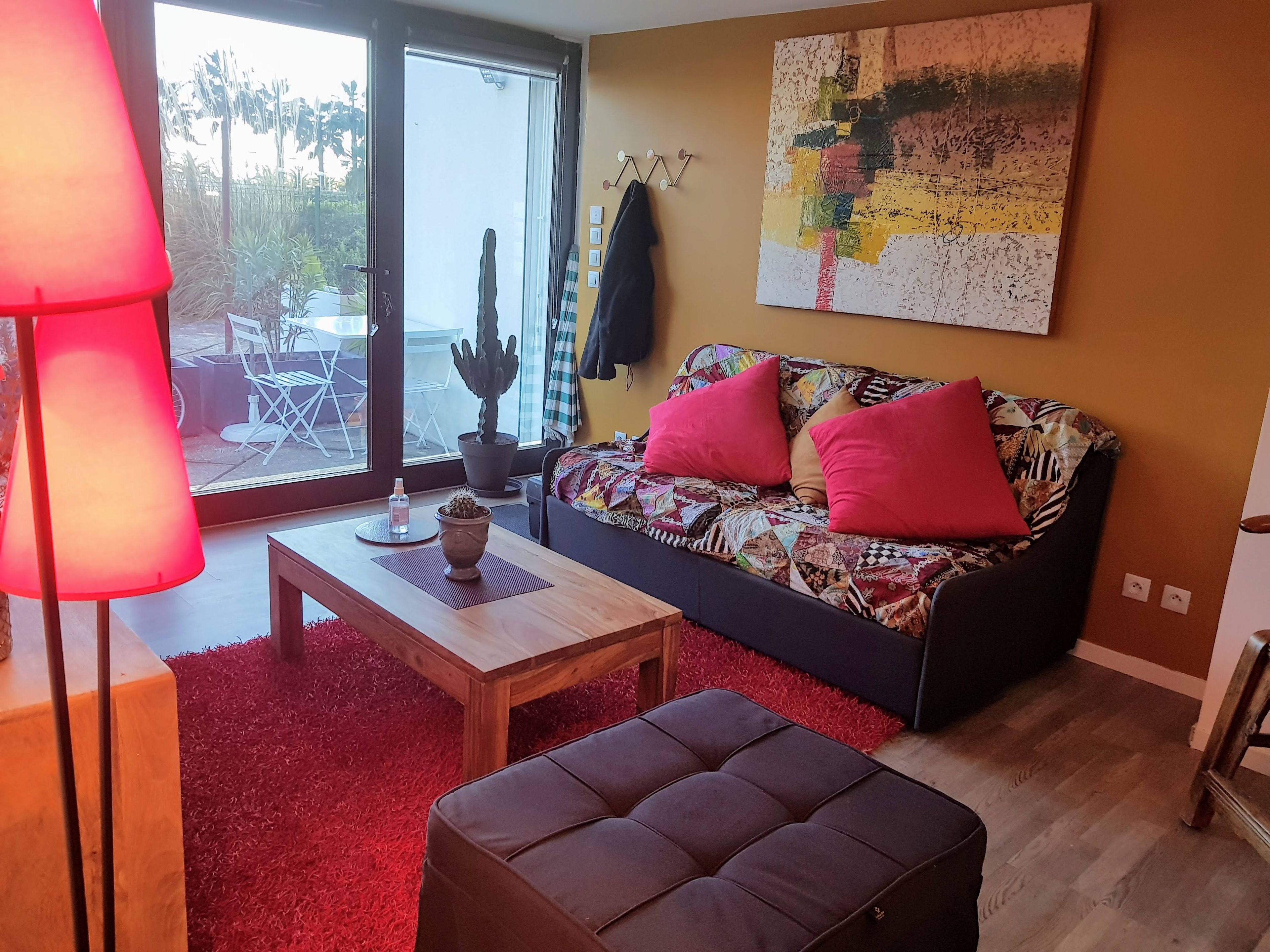 A living room with a sofa, a coffee table, a lamp, a cactus, and a view through a glass door.